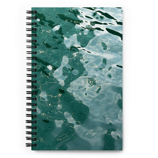 A spiral notebook with a soft-touch coating and a cover featuring a reflective, water-like pattern in shades of green and blue.